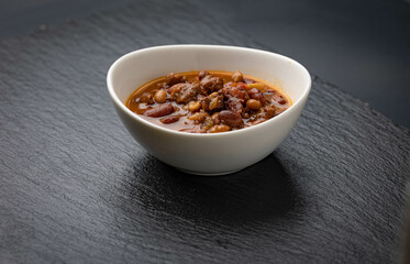 Bowl of chili on black stone background. Pinto beans, peppers, ground meat, onions and spices cooked in slow cooker.