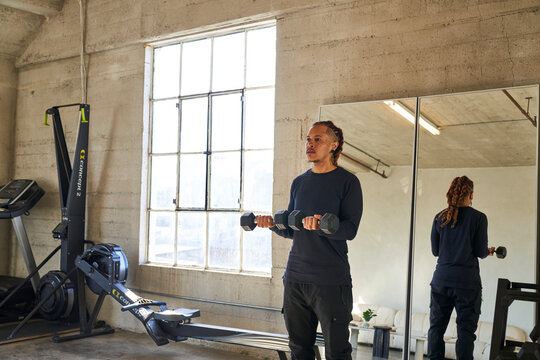man doing dumbbell curls with mirror and window in background