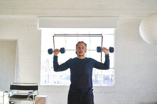 man with dumbbells at ear level with bright window in background