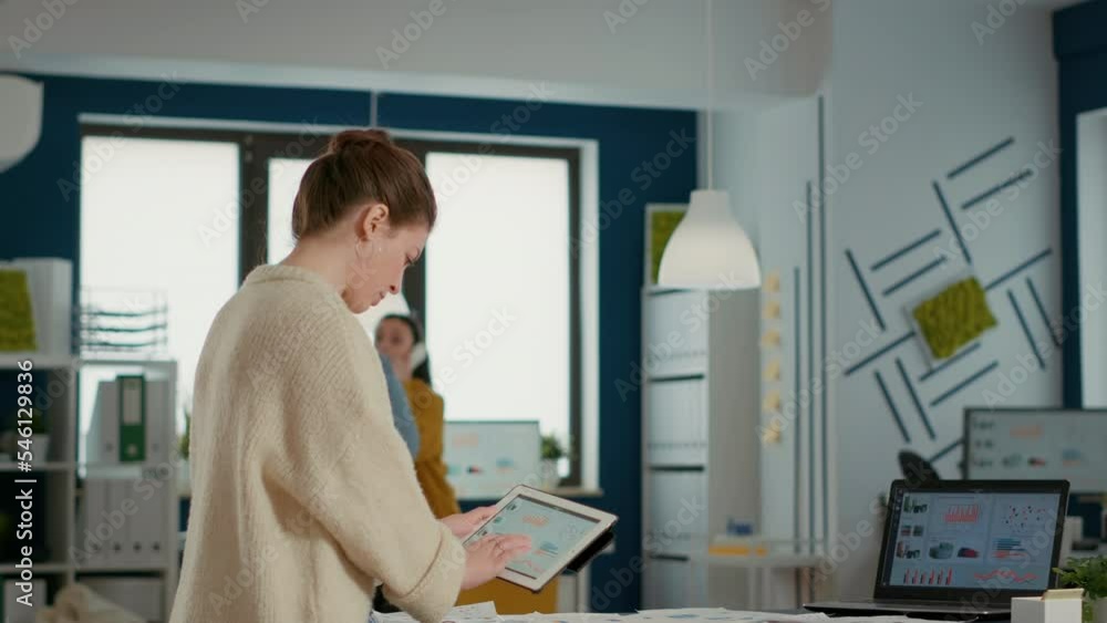 Poster woman holding digital tablet zooming in on sales pie chart and comparing data with statistics on lap