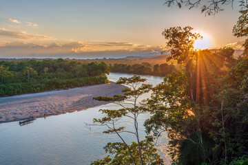 Panoramic top view on the Napo amazonian river during sunset with sunbeams over the lush forest and golden light on the river bank beach - Ecuador
