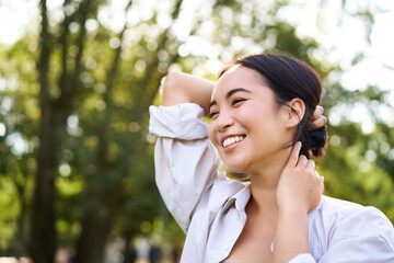 Beautiful young woman tying her hair while walking in park, smiling romantic, enjoying warm day