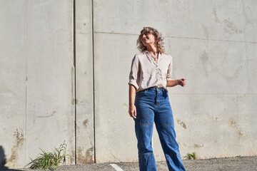 Obraz premium person posing in front of concrete wall in sun stands and looks back over shoulder