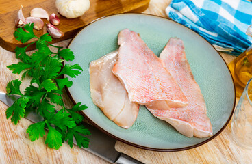 Fresh raw fillet of rockfish on plate with aromatic herbs and garlic on wooden table