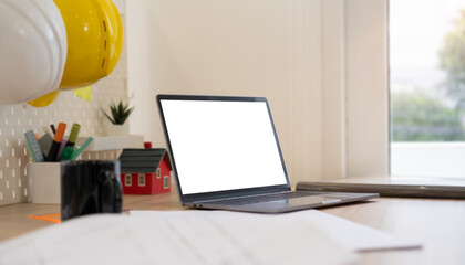 Laptop, safety helmet, blueprints, coffee cup and stationery on Architect or Engineer working desk.