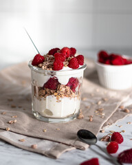 Dessert of granola, yogurt and raspberries in a glass glass on a white background