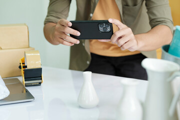Young male online business owner using cellphone checking parcel box.