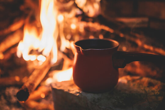 Warming up the fire, cozy winter night in the scandinavian cottage house cabin by the fireplace, burning fire with charcoal and firewood, heating up the drink beverage in the coffee pot