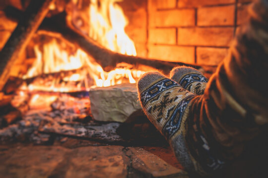 Warming up the fire, cozy winter night in the cabin house by the fireplace, fireplace burns in the scandinavian chalet cottage, burning fire with charcoal and firewood, view of woolen socks