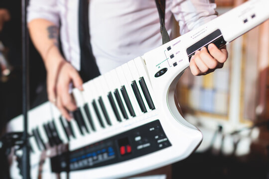 Concert view of a keytar synthesizer player with vocalist and musical jazz rock band orchestra performing in a background, electronic keyboard instrument guitar performer on a stage