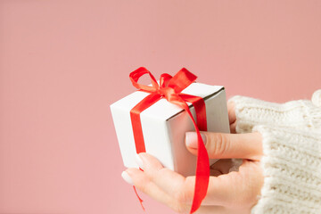 white gift box with red ribbon bow in woman hand with white sweater with copy space.