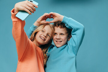 cute children stand on a blue background in bright clothes and a girl holds a smartphone in her...