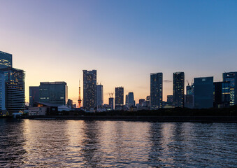 Tokyo tower through tall residential buildings along river at sunset