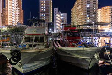 Fototapeta na wymiar Boats docked in harbor by residential towers at night