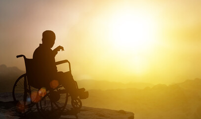 Fototapeta na wymiar Disabled man has a hope on wheelchair have sunset background. Challenge and Conquer success and health concept. Silhouette of person is sitting stretching hands out at sunset.