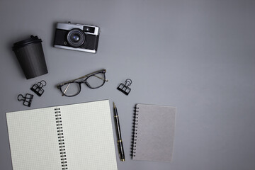 Black and white office times with camera, notebook, coffee cup and glasses on grey background.