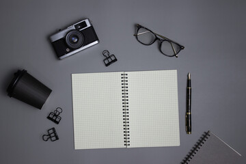 White notebook with camera, glasses and pen over the grey  background. 