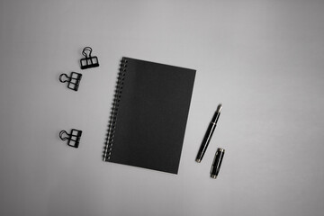 Black notebook, clips and pen over the grey background. 