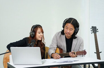 duo artists enjoy composing song melodies in the studio, a man with guitar is writing music sheet,...