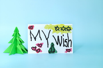 Christmas letter wish from kid concept. Closeup of written letter drawing beside a christmas tree.