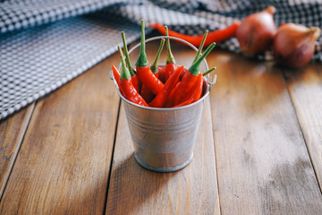 fresh red chilli in small bucket on wood desk and black tablecloth in the background with selective focus