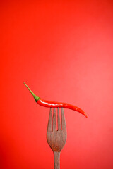 Fresh red chilli on wooden fork with red background