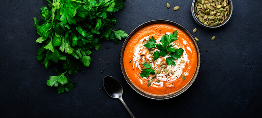 Hot spicy pumpkin soup puree with pumpkin seeds, cream, pepper and parsley. Winter or autumn healthy vegan vegetarian food. Soup bowl on black table background. Top view