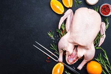 Raw whole duck with orange, pepper and rosemary. Ready to bake for a festive dinner. Black table background. Top view. Copy space - obrazy, fototapety, plakaty