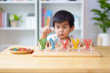 Blurred of asian 3 years old boy is learning to sorting the color rod to the glass, concept of homeschool, montessori, freedom, education, activity for child development and sensory activity for kid.