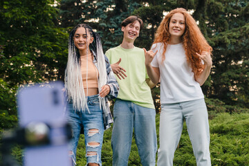 Contemporary people performing dancing challenge, recording themselves with a phone on a tripod in the park. Contemporary art. Doing silly dance moves. Internet