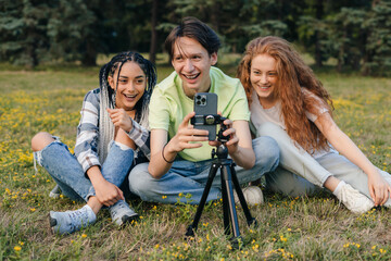 Naklejka na ściany i meble Group of friends taking selfie using a mobile phone on a tripod in the summer park. Summer nature. People lifestyle. Happy lifestyle.