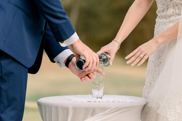 A bride and groom are pouring sand into a jar during their wedding ceremony.