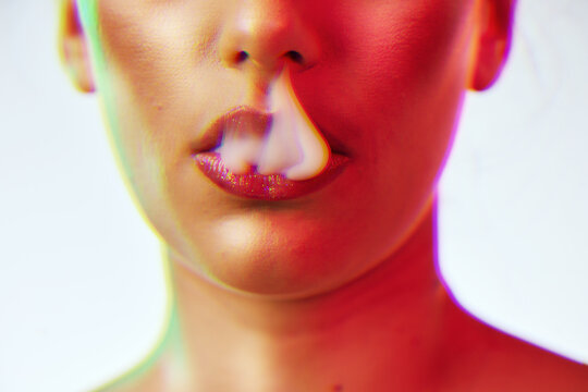 Beauty, cosmetics and woman lips with smoke with neon red lighting in studio on white background. Creative, artistic and half face of girl with makeup, lipstick and cyber aesthetic for smoking vape