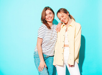 Two young beautiful smiling brunette hipster female in trendy summer clothes. Sexy carefree women posing near blue wall. Positive models having fun. Cheerful and happy