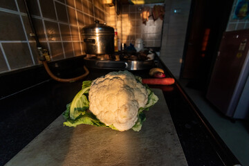 A raw uncut cauliflower on a cutting board in a kitchen.
