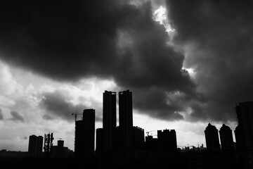 Black and white cityscape of silhouetted buildings and dark dramatic monsoon clouds in the sky above in the city of Mumbai.