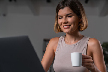Smiling businesswoman in casual wear typing on laptop drinking coffee