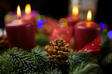 Shallow focus pine cone on advent wreath with four lit candles and decor