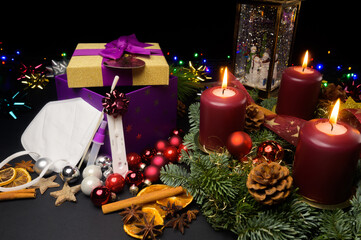 Mask and COVID test kit leaning on gift box next to advent wreath and snow globe