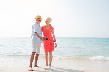 Happy senior couple using smart phone together on the beach having fun in a sunny day, activity after retirement in vacations and summer.