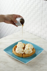 Waffles with whipped butter on a plate, syrup being poured