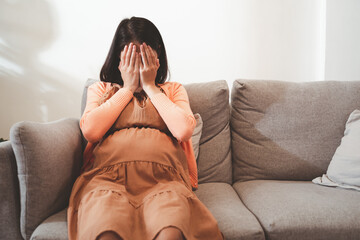 Young pregnant asian woman has suffering from headache sitting on sofa. Pregnancy symptoms