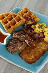 Breakfast platter with bacon, hash brown, beef burger patty, scrambled egg and waffles