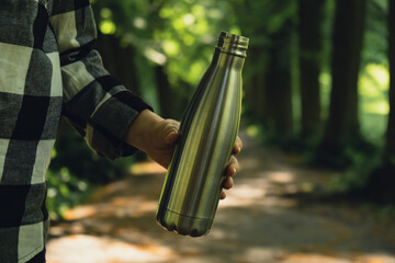Close-up of Unrecognizable female hand holding Water bottle. Reusable steel thermo water bottle in...
