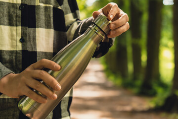 Close-up of Unrecognizable female hand holding Water bottle. Reusable steel thermo water bottle in...