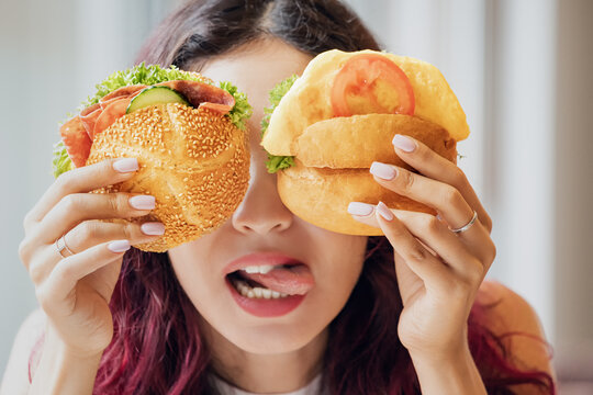 A girl in a cafe fooling around and closed her eyes with two cheeseburgers. Fast food and healthy diet concept