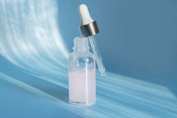 Glass cosmetic bottle dropper with beuty oil or serum for skin care on blue background. Natural skin care concept. Hard shadows