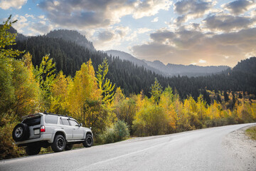 White 4x4 car traveling along a autumn mountains road.