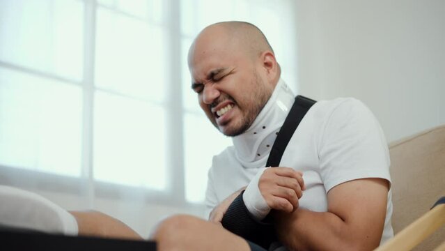 Man suffered pain from accident fracture broken bone injury with leg splints in cast, neck splints collar, arm splints, sling support arm in living room. Social security and health insurance concept.