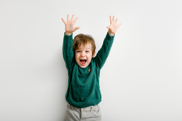 Cute little boy with raised hands up with happiness on white wall background - obrazy, fototapety, plakaty